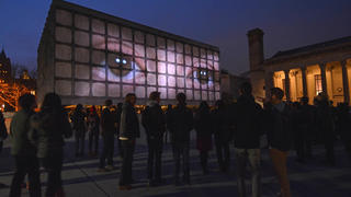 Crowd looking at giant light box on building of human eyes