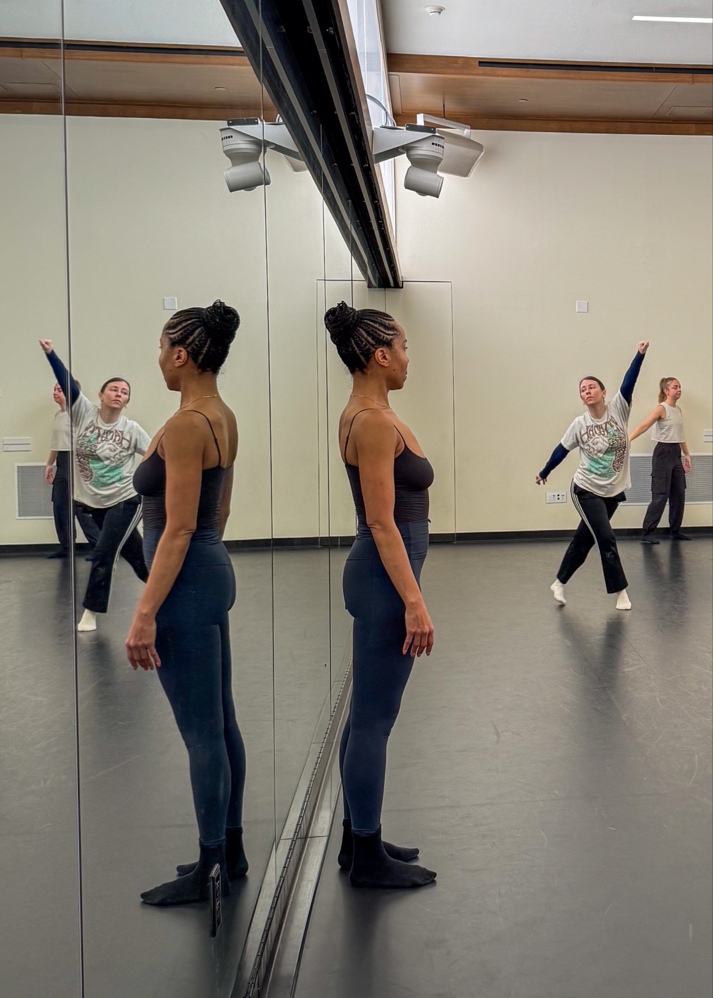 Instructor Sidra Bell watches students practicing dance in the studio, surrounded by large mirrors reflecting their movements.