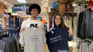 Man holding a t-shirt reading "Boola Boola" and woman holding a t-shirt reading "50 Women at Yale 150"